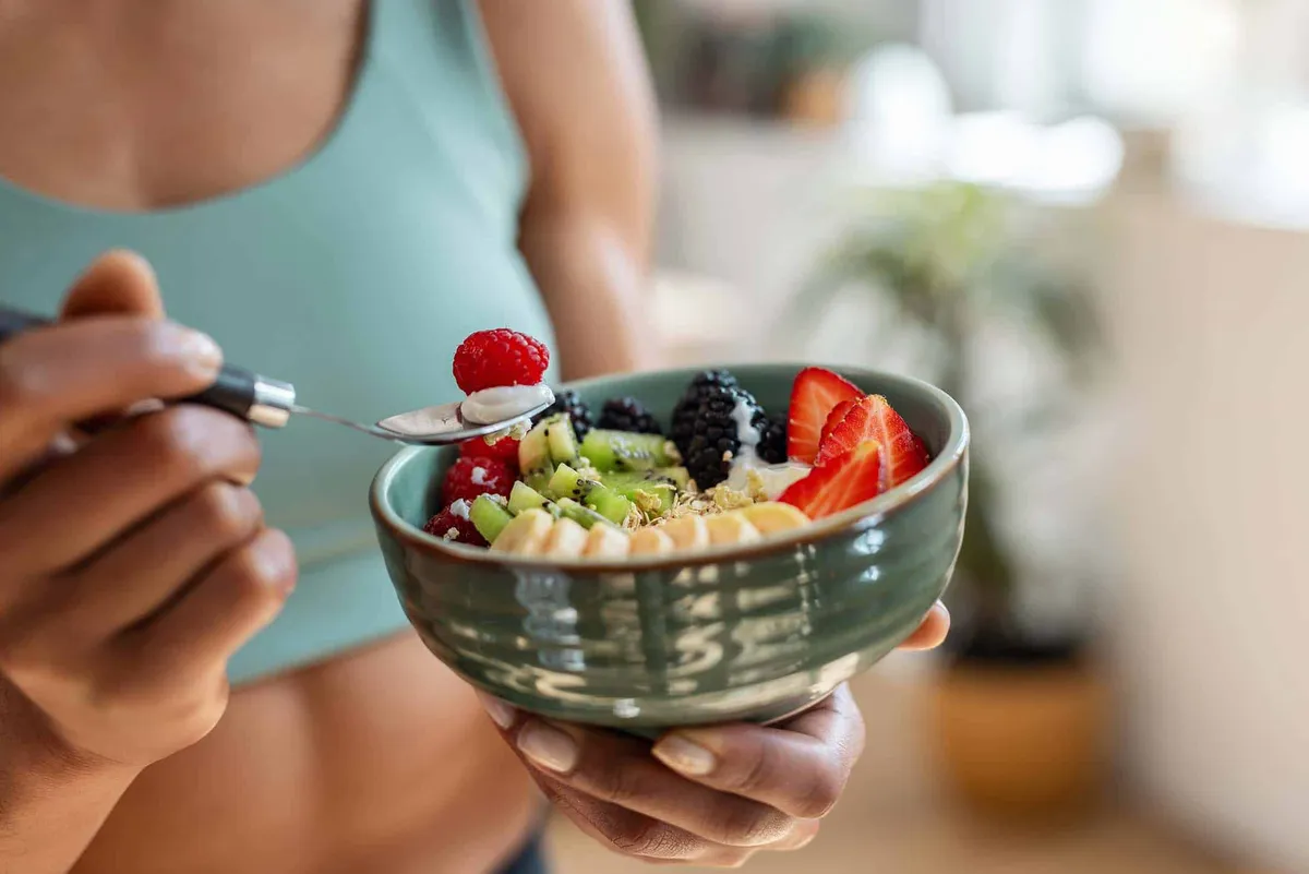 Pregnant woman eating a bowl of fresh berries, kiwi and granola with a spoon