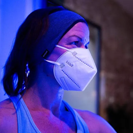 A woman in protective gloves, beanie and mask walking out of a cryotherapy chamber through billowing cold mist