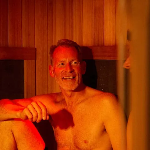 An older man smiles while sitting in the infrared sauna, one arm resting on his raised knee