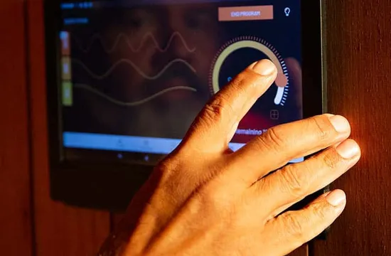 A hand adjusts the touchscreen control panel of an infrared sauna, showing session settings and a temperature dial