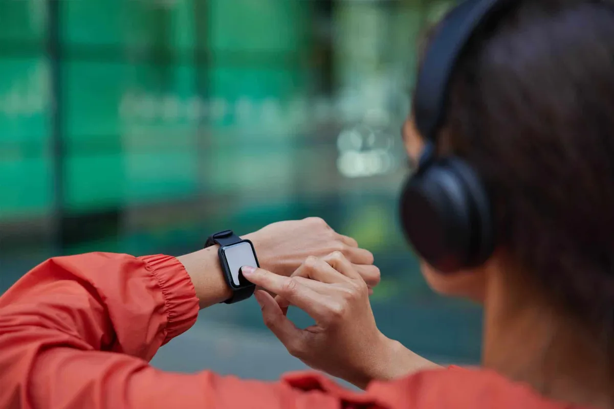 A woman wearing headphones checks her smartwatch while exercising outdoors