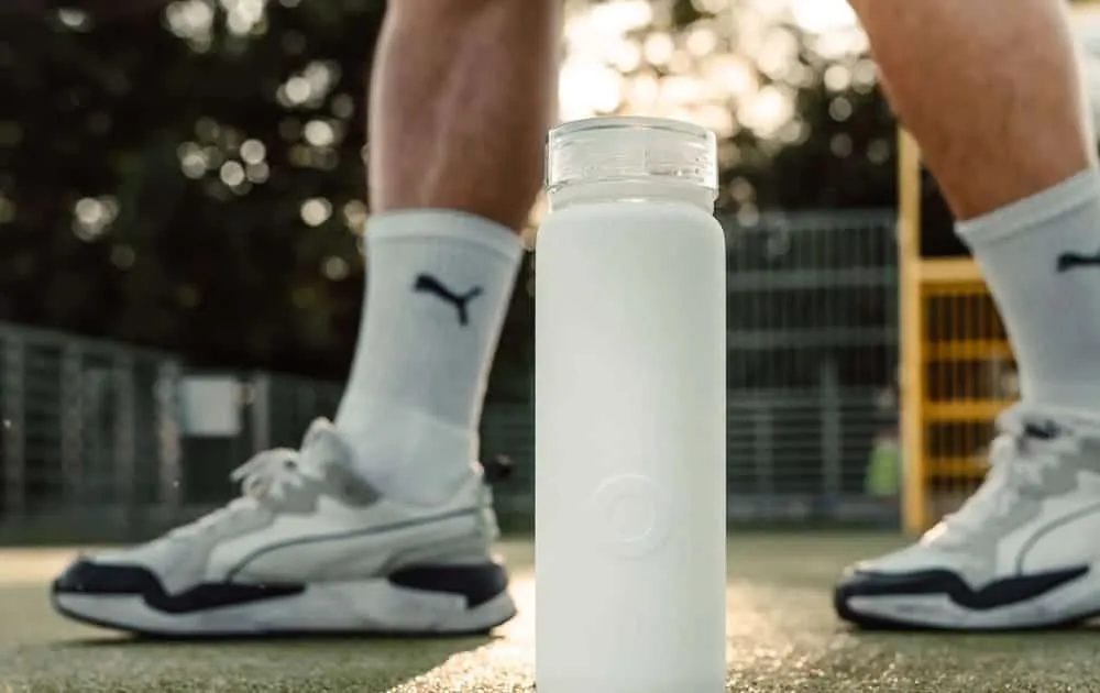 White water bottle standing on an outdoor sports court with a runner's legs behind it