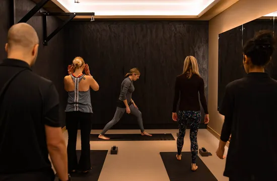 A group yoga class moves through a lunging stretch on mats in a dark-panelled studio at The FIT Partnership