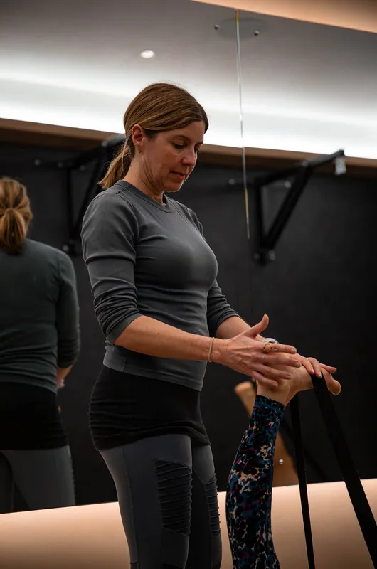 A yoga instructor uses a strap to guide a client's stretched leg during a one-on-one session