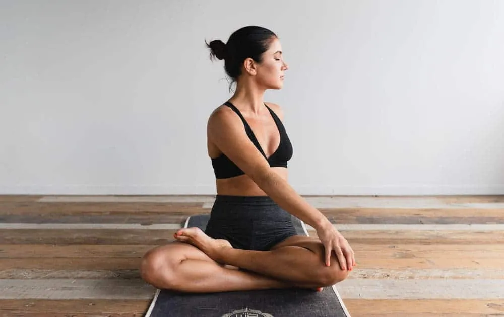 Woman sitting cross-legged in a meditative yoga pose on a mat in a bare studio